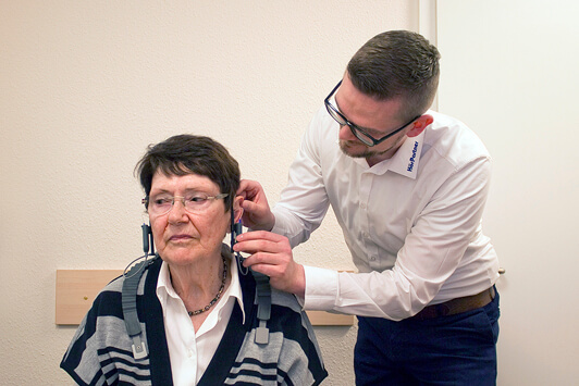 Ein Hörakustiker passt einer älteren Frau ein Hörgerät im Hörzentrum an.