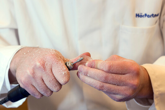 Ein Hörakustiker bearbeitet ein Hörgerät handwerklich für eine individuelle Anpassung.