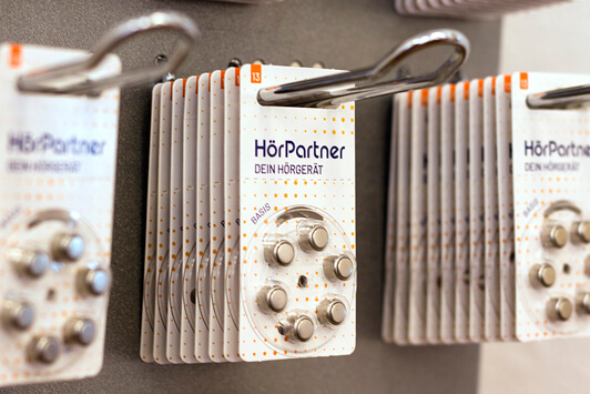 Hörgerätebatterien von HörPartner in Blisterverpackungen hängen ordentlich an einer Wand.